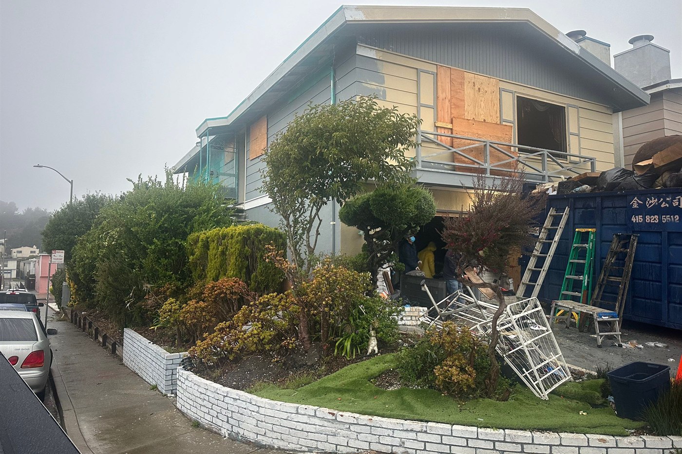 The same house before renovation: windows boarded over, siding stripped back and a debris dumpster in the driveway